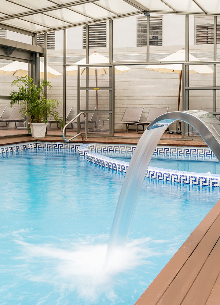 Piscina interior pequeña con una cascada suave, rodeada de tumbonas y sombrillas.