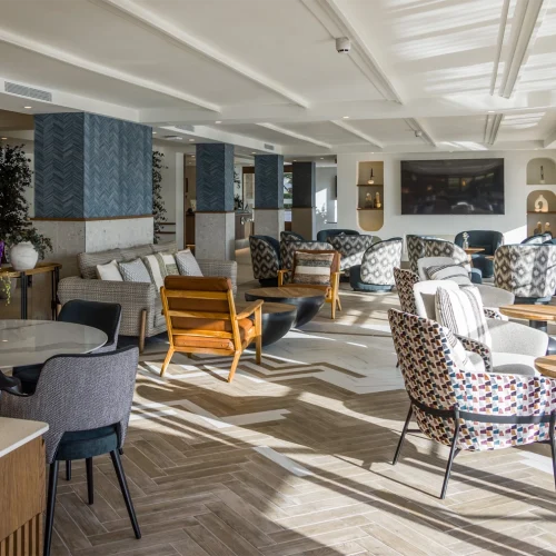 The image shows a modern, spacious, and elegant living room with a variety of seating options. The room features a blend of contemporary and mid-century modern design elements, characterized by clean lines, geometric patterns, and a mix of textures.