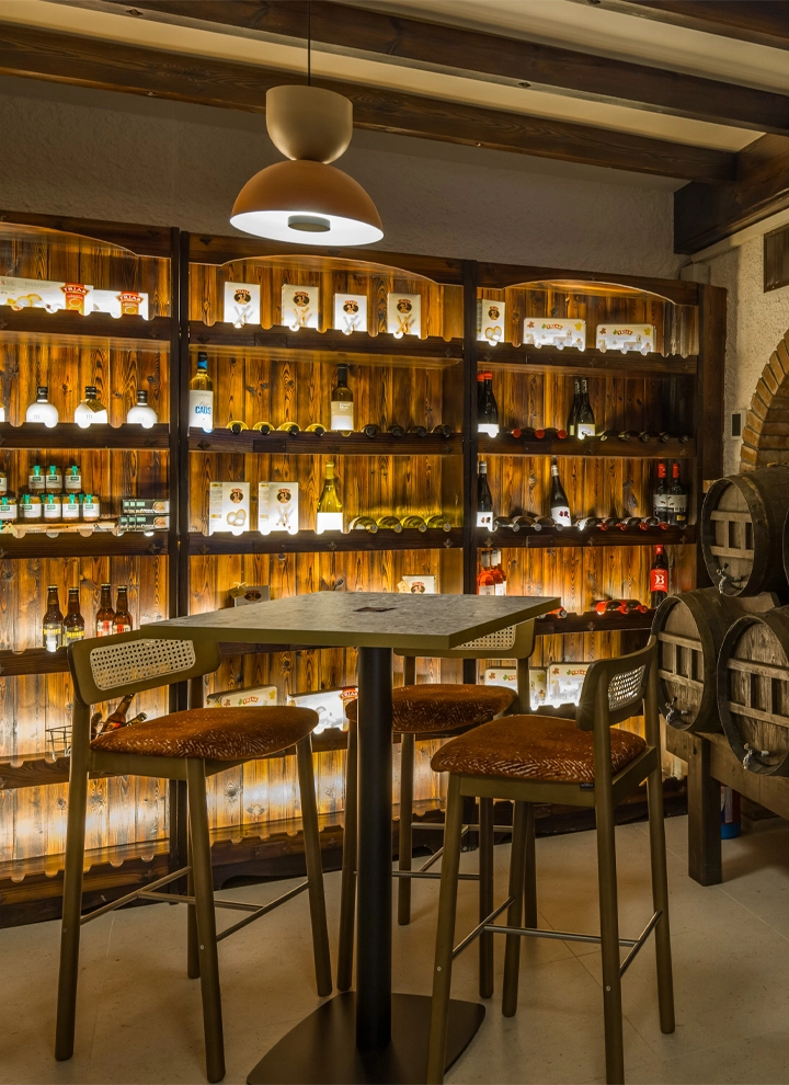 Cellar room with high tables and shelves elegantly filled with wine bottles, softly lit by ambient lighting.