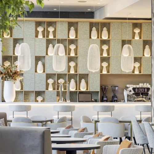 Coffee shop with hanging lamps from the ceiling, decorated with plants around and shelves with white geometric vases.