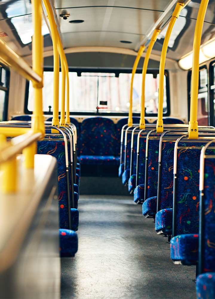 El interior de un autobús de dos pisos visto desde la parte trasera, con una fila de asientos vacíos y pasamanos amarillos que se extienden a lo largo.