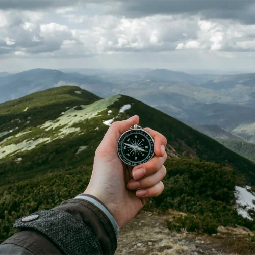A mountain landscape with a hand in the foreground holding a compass.