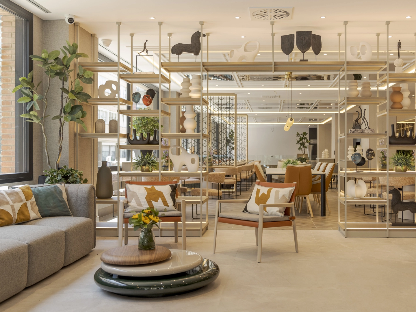 Interior del hotel ILUNION Romareda con estanterías, plantas, sillones y una mesa con flores.