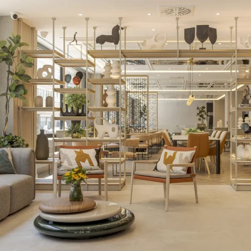 Indoor space of ILUNION Romareda Hotel featuring bookshelves, plants, armchairs, and a table with flowers.