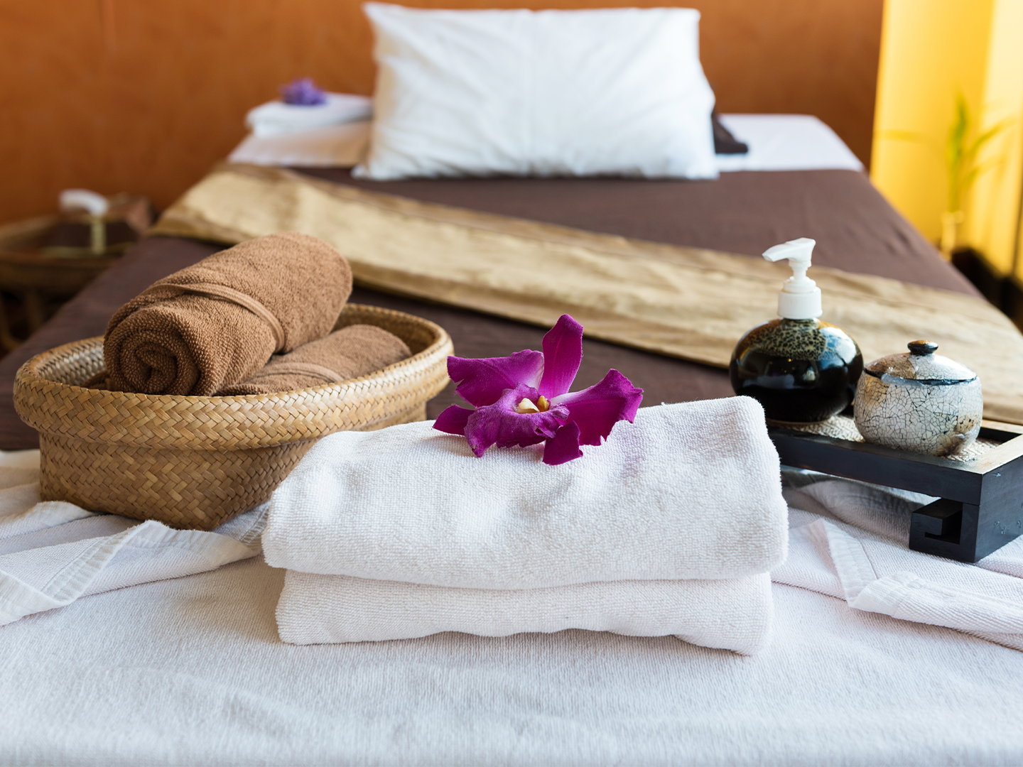 Cama de masaje cubierta con toallas y decorada con una flor, rodeada de frascos de productos de spa.