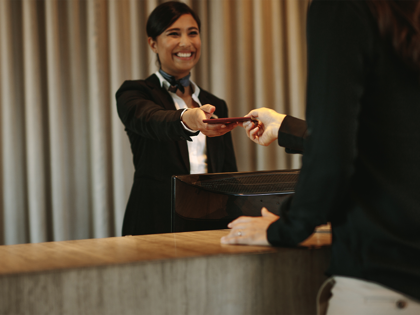 Recepcionista de hotel entregando a otra persona detrás de un mostrador.