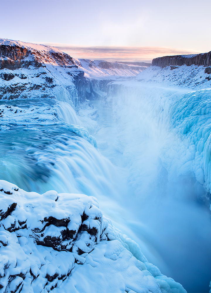 Paisaje de Islandia con una cascada congelada entre rocas y nieve en un paisaje blanco, bajo cielo claro.