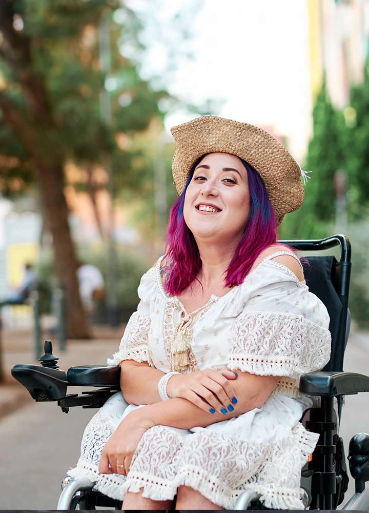 Smiling young woman with red and blue hair posing in a wheelchair.