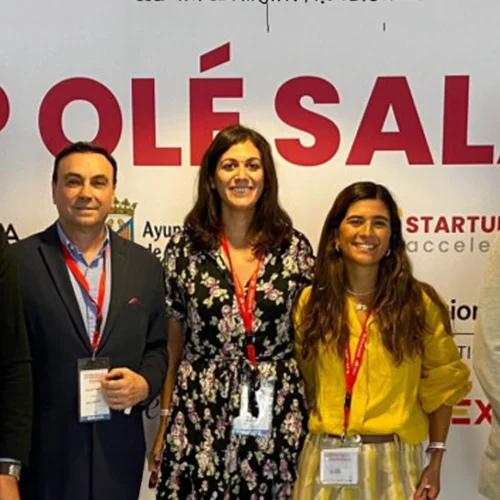Five people pose together in front of a large white sign with red letters that read “STARTUP OLÉ SALAMANCA.”
