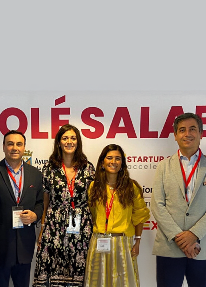 Four people pose together in front of a large white sign with red letters that read “STARTUP OLÉ SALAMANCA.”