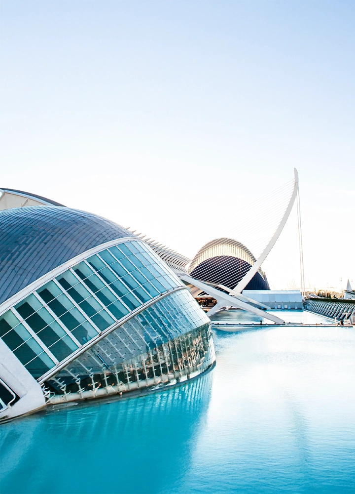 Edificios de arquitectura moderna de la Ciudad de las Artes y las Ciencias de Valencia. En primer plano, el Hemisfèric se refleja en el agua, con el puente de l'Assut de l'Or de fondo.