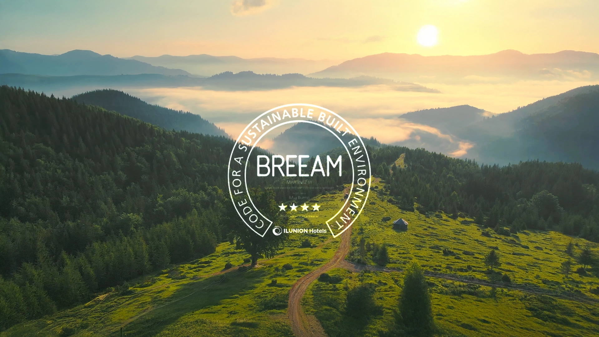 Vista panorámica del amanecer en un valle montañoso cubierto de niebla y bosques. Un camino rural asciende por una colina en primer plano. Un sello de certificación BREEAM está sobrepuesto.