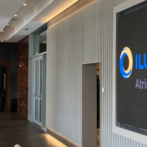 Modern and bright room with tables, small plants, hanging lamps, and a screen displaying the text “ILUNION Hotels Atrium.”