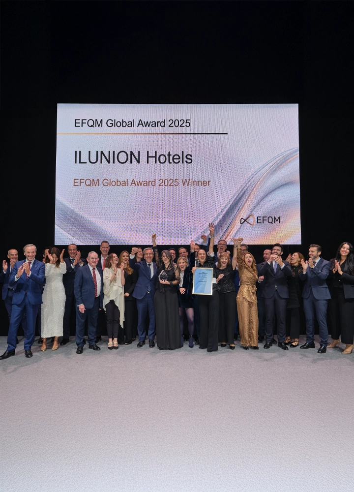 Gran grupo de personas celebrando en un escenario con cartel que indica ILUNION Hotels ganador del EFQM Global Award 2025.