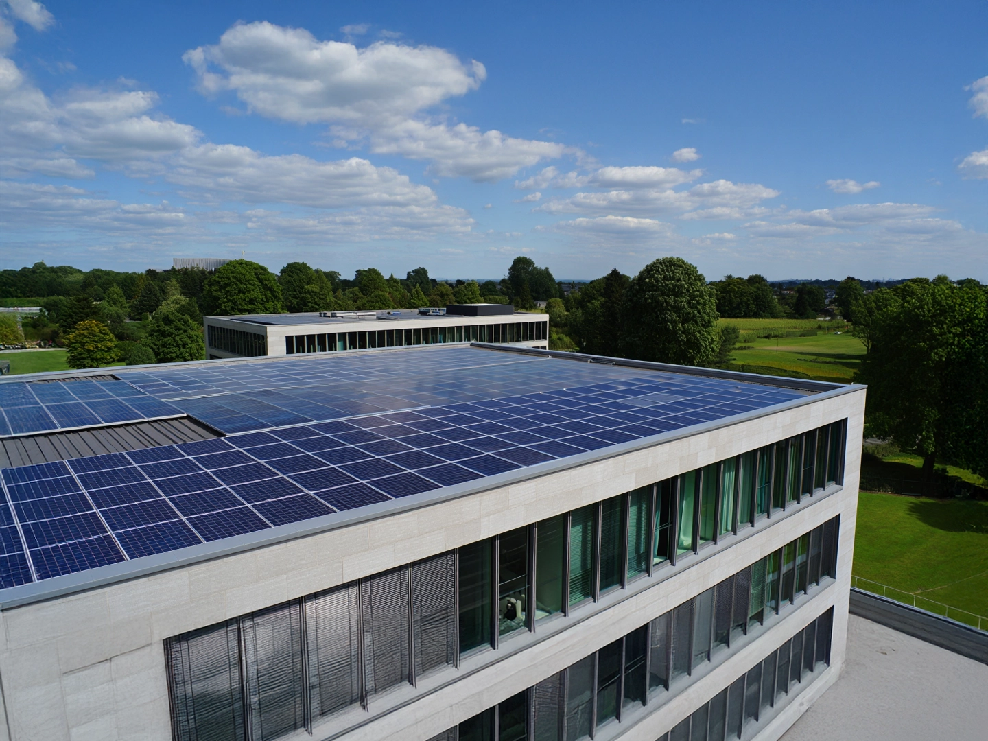 Edificio moderno con paneles solares en el tejado, rodeado de zonas verdes y cielo parcialmente despejado.