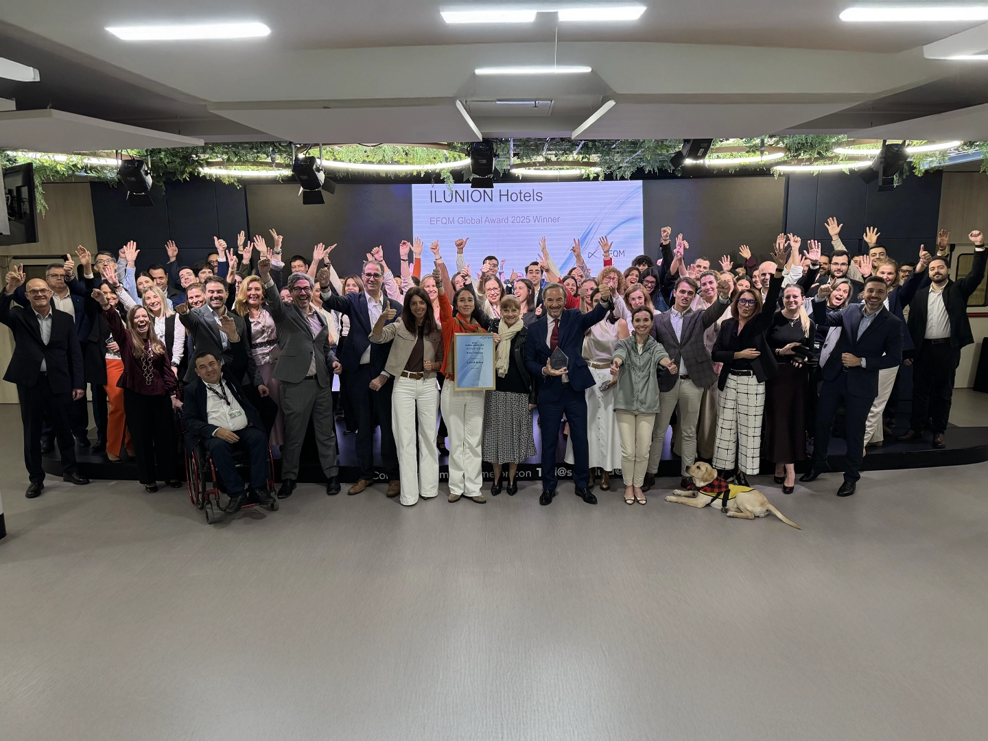 Gran grupo de personas celebrando en un escenario con cartel que indica ILUNION Hotels ganador del EFQM Global Award 2025.