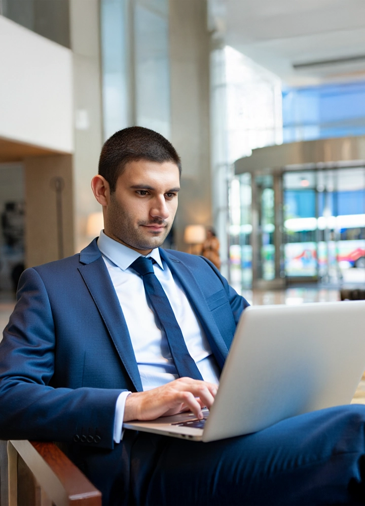 Persona con traje usando portátil en oficina moderna con grandes ventanales, en contexto profesional o de trabajo.