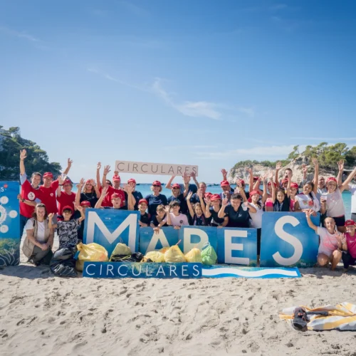 Grupo en playa con bolsas recolectadas, sostienen letras 'MARES' y pancarta 'CIRCULARES' en jornada de limpieza ambiental.