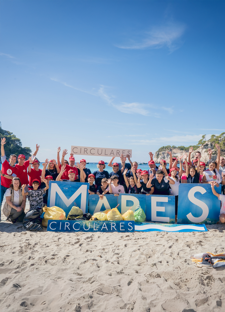Grupo en playa con bolsas recolectadas, sostienen letras 'MARES' y pancarta 'CIRCULARES' en evento de conservación ambiental.
