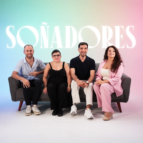 Cuatro personas sentadas en un sofá gris frente a fondo pastel con la palabra 'SOÑADORES' en grande sobre ellos.