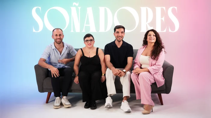 Cuatro personas sentadas en sofá gris frente a fondo degradado azul-rosa con la palabra 'SOÑADORES' en letras blancas.