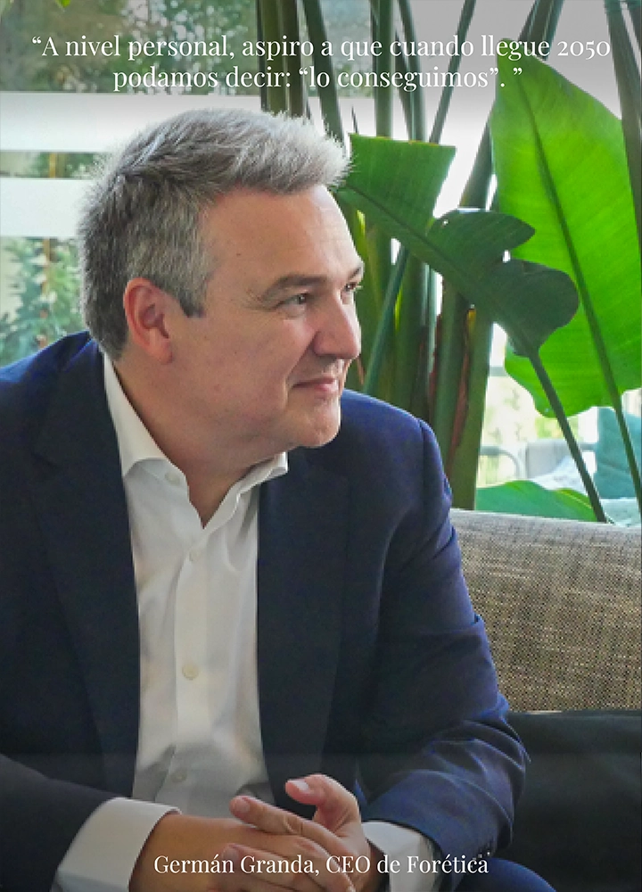 Hombre sentado en un sofá con plantas decorativas al fondo, vistiendo traje oscuro y camisa blanca. Texto visible en la imagen: Parte superior: