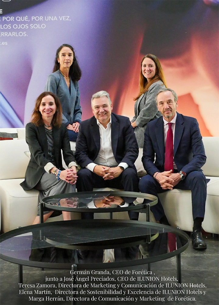 Cinco personas sentadas y de pie en un espacio interior con sofás y mesas, posando para una foto corporativa frente a un fondo con texto promocional. Texto en la parte inferior: Germán Granda, CEO de Forética, junto a José Ángel Preciados, CEO de ILUNION Hotels. Teresa Zamora, Directora de Marketing y Comunicación de ILUNION Hotels. Elena Martín, Directora de Sostenibilidad y Excelencia de ILUNION Hotels. Marga Herrán, Directora de Comunicación y Marketing de Forética.