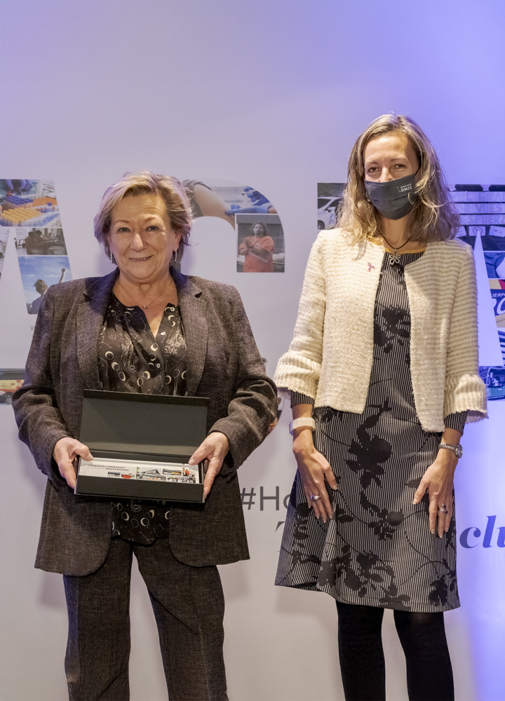 Two people standing; one holds a rectangular box. Background with large letters containing images.