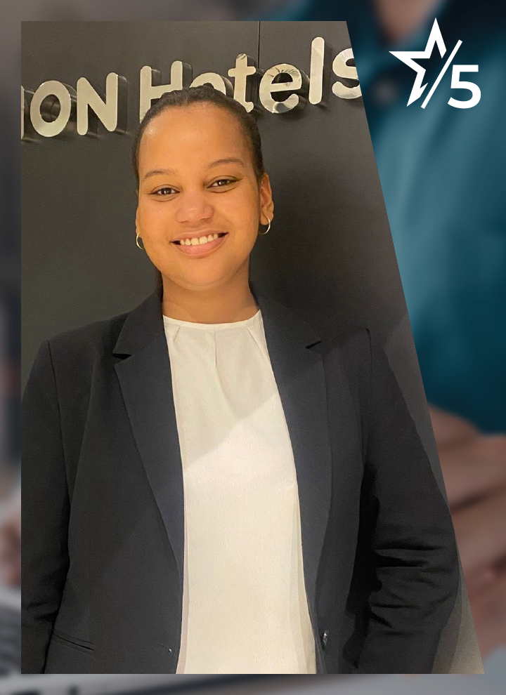 Una mujer sonriente con americana negra y blusa blanca posa frente a una pared.. En la esquina superior aparece una estrella con el número 5, que sugiere reconocimiento o excelencia. La imagen transmite profesionalidad y destaca el vínculo con el sector hotelero.