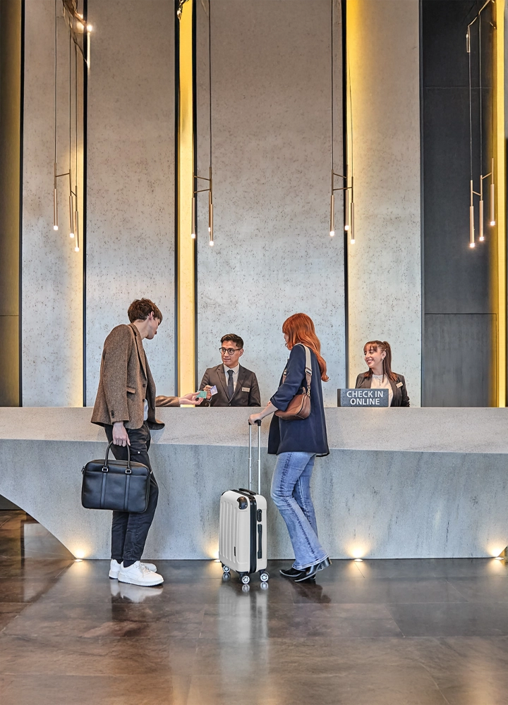 Recepción de hotel moderna con atención presencial y opción digital, en un entorno cálido, funcional y accesible.