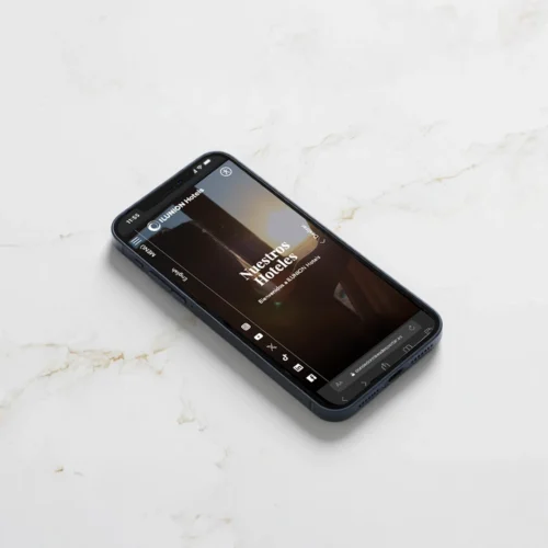 Un smartphone situado sobre una superficie de mármol blanco mostrando la página web de ILUNION Hotels. En la pantalla se lee 