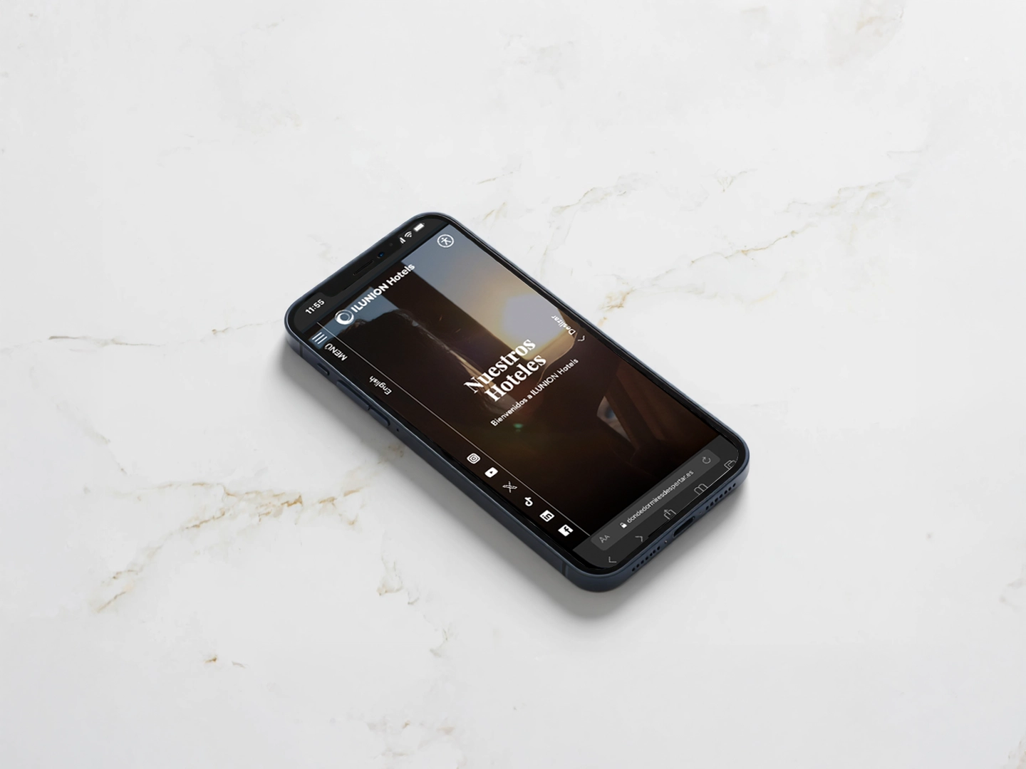 Un smartphone situado sobre una superficie de mármol blanco mostrando la página web de ILUNION Hotels. En la pantalla se lee "Nuestros Hoteles - Bienvenidos a ILUNION Hotels" sobre una imagen cálida, con la barra de navegación lateral y la URL "dondedormiresdespertar.es" visible en el navegador.