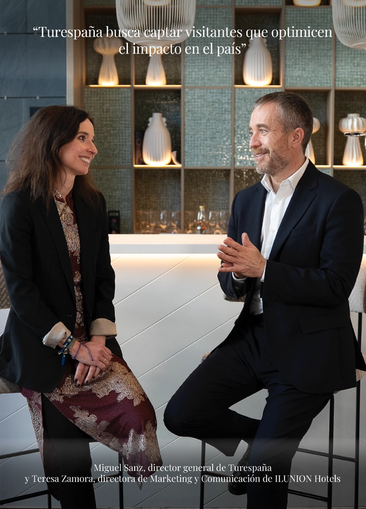 Fotografía de Teresa Zamora, directora de Marketing de ILUNION Hotels, y Miguel Sanz, director de Turespaña, conversando de forma relajada en el área de un bar moderno. En la parte superior, destaca el texto: 