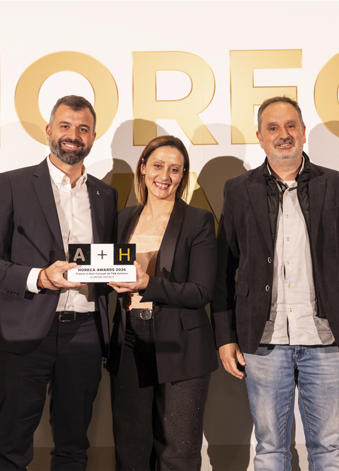 Tres personas posando sonrientes frente a un fondo blanco con letras doradas grandes que forman parte de la palabra 