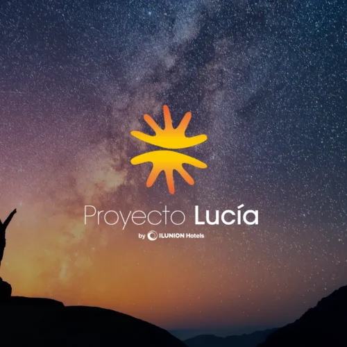 Composición visual con un cielo nocturno estrellado y la Vía Láctea de fondo. En la esquina inferior izquierda, se ve la silueta de una persona sobre una roca señalando hacia el cielo. En el centro, destaca el logotipo del 'Proyecto Lucía' compuesto por un icono solar amarillo y naranja, seguido del texto 'Proyecto Lucía by ILUNION Hotels'. El horizonte muestra siluetas de montañas bajo una luz cálida de atardecer o amanecer.