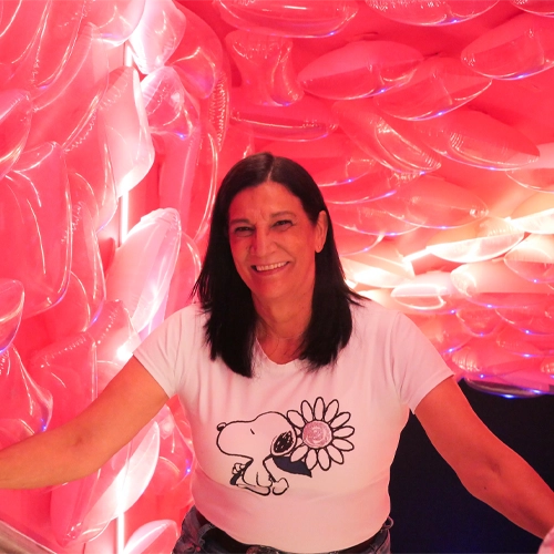 Persona con camiseta blanca estampada con Snoopy y una flor, posando en un espacio iluminado por luces rosadas intensas con formas acolchadas y curvas en las paredes que crean un ambiente envolvente y artístico.