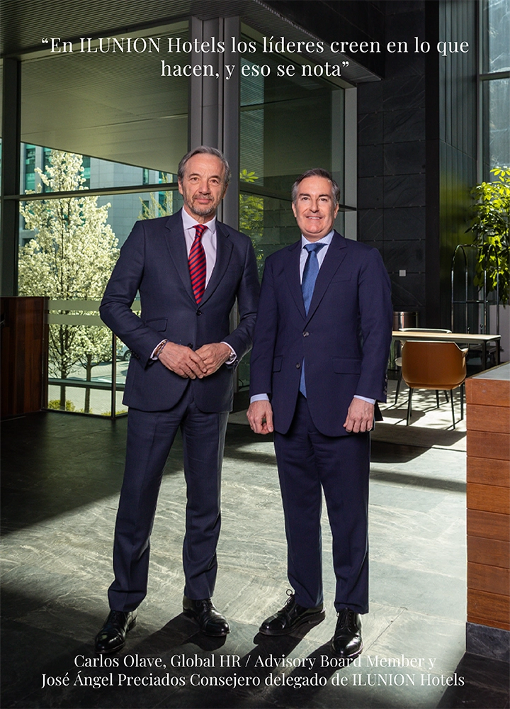 Dos personas de pie con traje formal en el interior de un espacio moderno y luminoso, con grandes ventanales, plantas y mobiliario elegante que transmiten un entorno corporativo y profesional. En la parte superior se lee la cita “En ILUNION Hotels los líderes creen en lo que hacen, y eso se nota”. En la parte inferior aparece el texto “Carlos Olave, Global HR / Advisory Board Member y José Ángel Preciados, Consejero delegado de ILUNION Hotels”, reforzando un mensaje de liderazgo, confianza y cultura empresarial.