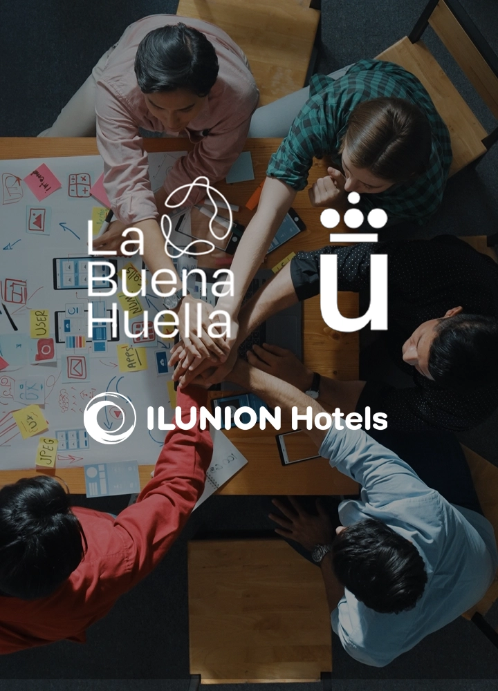 Vista cenital de cinco personas con las manos juntas sobre una mesa de madera con notas adhesivas, esquemas y rotuladores. Sobre la imagen aparecen los textos “La Buena Huella” y “ILUNION Hotels”, junto a un icono con una “ü”.