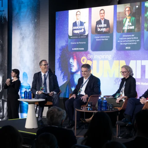 Mesa redonda en un evento con varias personas sentadas en sillones sobre un escenario. A la izquierda hay una persona intérprete de lengua de signos. En el fondo, una gran pantalla muestra fotos y nombres de los ponentes bajo el título “Be inspiring Summit”.