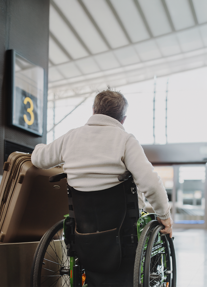 La imagen muestra a una persona usuaria de silla de ruedas desplazándose por el interior de una terminal de transporte, junto a varias maletas y próxima a una señal identificada con el número “3”. El espacio cuenta con amplias zonas de circulación, accesos adaptados y una arquitectura diseñada para facilitar la movilidad de las personas viajeras. La presencia del equipaje y de las instalaciones de transporte sitúa la escena en un contexto de desplazamiento y turismo, destacando la importancia de disponer de entornos accesibles que favorezcan la autonomía durante el viaje. En conjunto, la fotografía transmite valores de accesibilidad, inclusión e igualdad de oportunidades, promoviendo una experiencia de movilidad cómoda y sin barreras para todas las personas.
