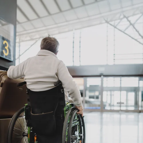 La imagen muestra a una persona usuaria de silla de ruedas desplazándose por el interior de una terminal de transporte, junto a varias maletas y próxima a una señal identificada con el número “3”. El espacio cuenta con amplias zonas de circulación, accesos adaptados y una arquitectura diseñada para facilitar la movilidad de las personas viajeras. La presencia del equipaje y de las instalaciones de transporte sitúa la escena en un contexto de desplazamiento y turismo, destacando la importancia de disponer de entornos accesibles que favorezcan la autonomía durante el viaje. En conjunto, la fotografía transmite valores de accesibilidad, inclusión e igualdad de oportunidades, promoviendo una experiencia de movilidad cómoda y sin barreras para todas las personas.