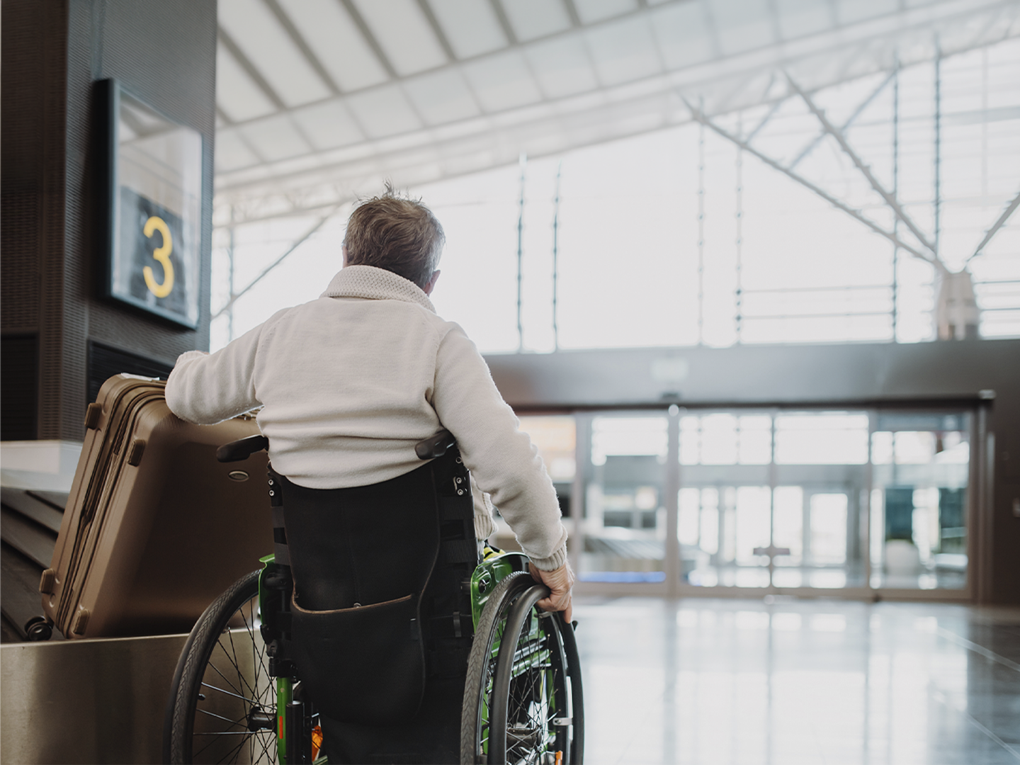 La imagen muestra a una persona usuaria de silla de ruedas desplazándose por el interior de una terminal de transporte, junto a varias maletas y próxima a una señal identificada con el número “3”. El espacio cuenta con amplias zonas de circulación, accesos adaptados y una arquitectura diseñada para facilitar la movilidad de las personas viajeras. La presencia del equipaje y de las instalaciones de transporte sitúa la escena en un contexto de desplazamiento y turismo, destacando la importancia de disponer de entornos accesibles que favorezcan la autonomía durante el viaje. En conjunto, la fotografía transmite valores de accesibilidad, inclusión e igualdad de oportunidades, promoviendo una experiencia de movilidad cómoda y sin barreras para todas las personas.