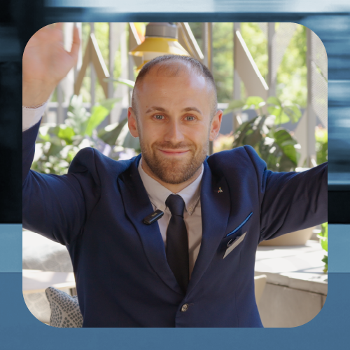 Persona con traje azul marino y corbata posa frente a la cámara con ambos brazos levantados. Se encuentra en un espacio interior luminoso con plantas y grandes ventanales al fondo. La imagen está enmarcada dentro de un diseño gráfico con bordes redondeados y tonos azules.