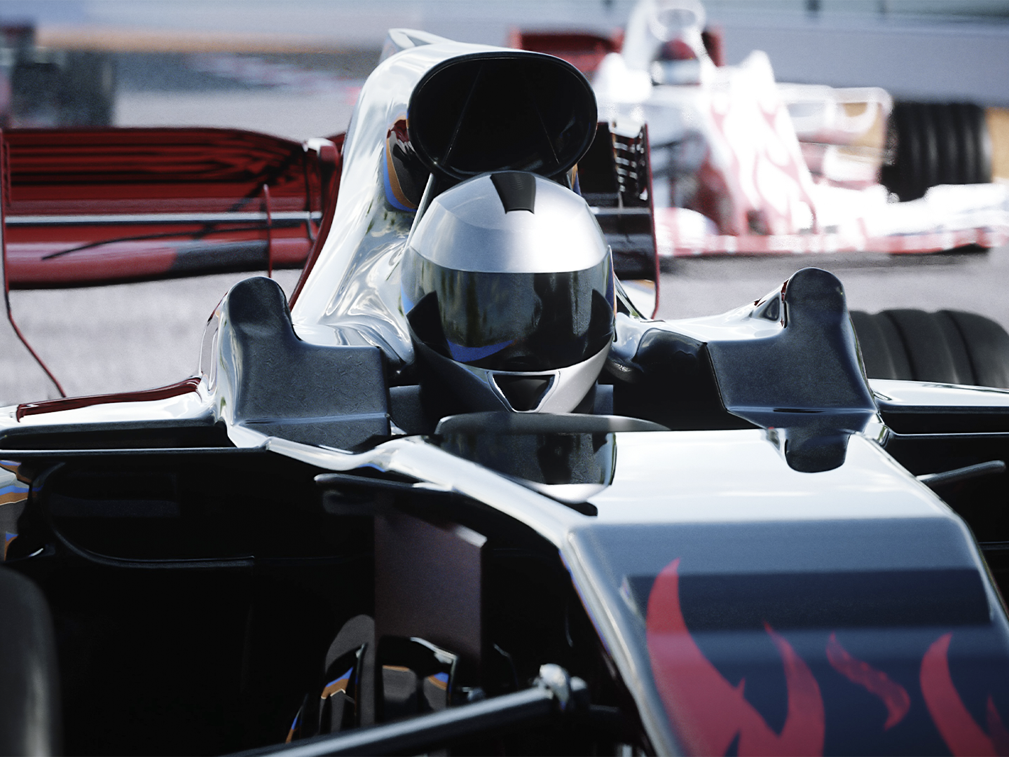 Primer plano frontal de un monoplaza de competición en un circuito de carreras. El vehículo presenta una carrocería aerodinámica en colores negro, plata y rojo, con un casco de piloto visible en el habitáculo. Destacan el alerón delantero, las tomas de aire superiores y los neumáticos anchos característicos de este tipo de vehículos. Al fondo aparece otro monoplaza desenfocado, reforzando el contexto de competición automovilística. La iluminación resalta las superficies brillantes y las líneas técnicas del vehículo, que ocupa casi toda la imagen.