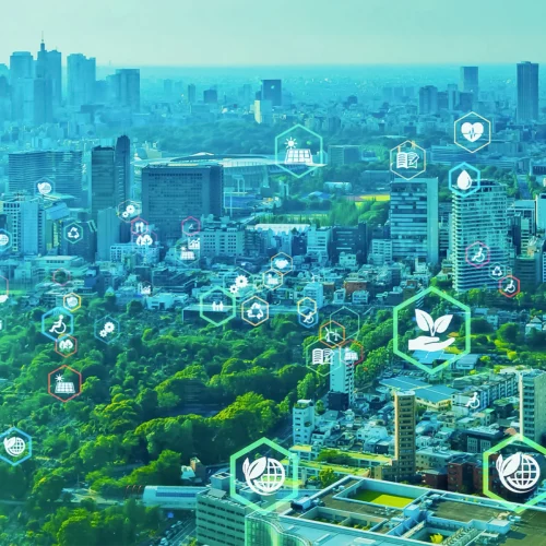 Vista aérea de una gran ciudad con amplias zonas verdes integradas entre edificios y rascacielos. Sobre el paisaje aparecen iconos semitransparentes relacionados con sostenibilidad, reciclaje, energías renovables, salud, educación, movilidad y eficiencia energética. La composición crea una representación visual de una ciudad inteligente y sostenible, combinando naturaleza, desarrollo urbano y tecnología sobre un fondo en tonos verdes y azules.