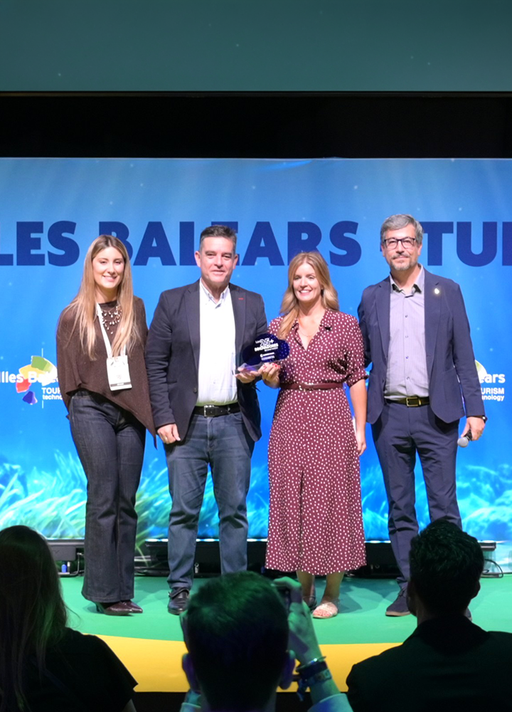 Cuatro personas posan con un premio sobre un escenario, ante una pantalla azul con el texto «Les Balears».