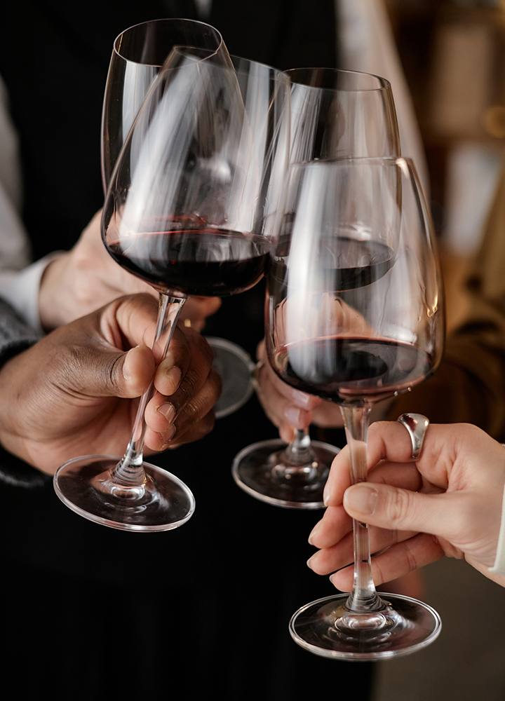 Brindis con copas de vino tinto sostenidas por varias personas, reunidas en torno a una mesa.